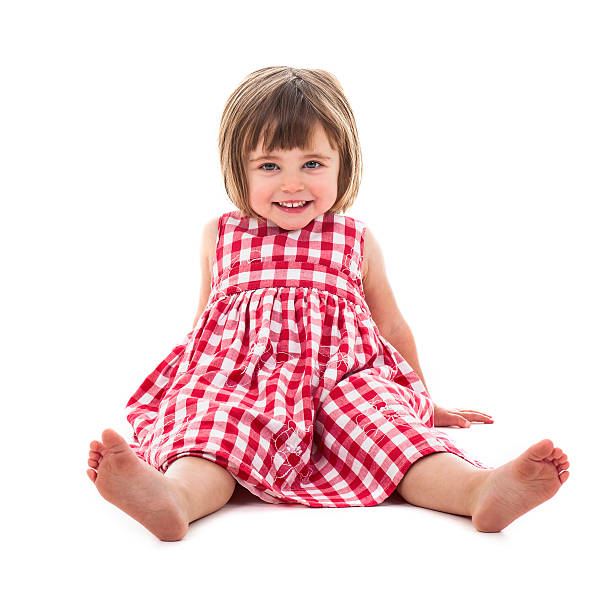 Toddler in red chequered dress lying against white stock photo