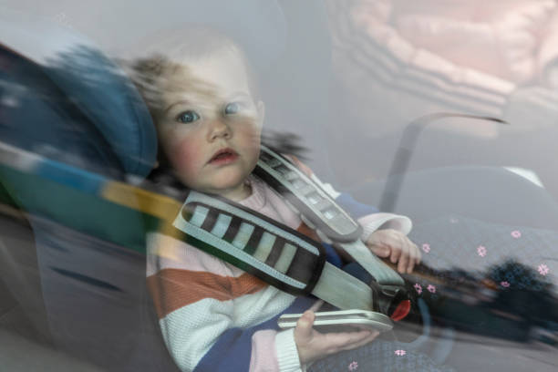 Toddler inside car sitting with phone in hand looking out of the window stock photo