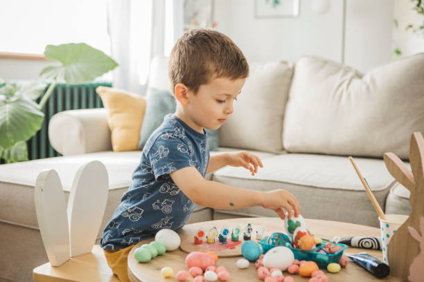 Toddler is happy about Easter Toddler painting eggs for Easter at home. easter sunday stock pictures, royalty-free photos & images