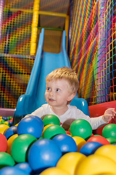 Toddler with hearing aid slides into ball pool stock photo