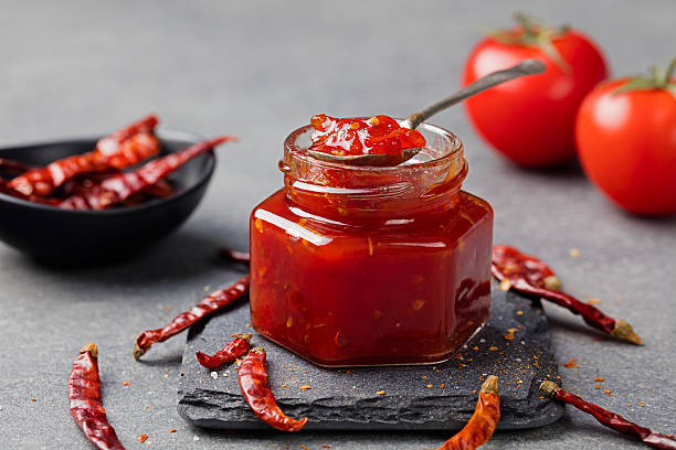 Tomato and chili sauce, jam, confiture in a glass jar Tomato and chili sauce, jam, confiture in a glass jar on a grey stone background. chutney stock pictures, royalty-free photos & images