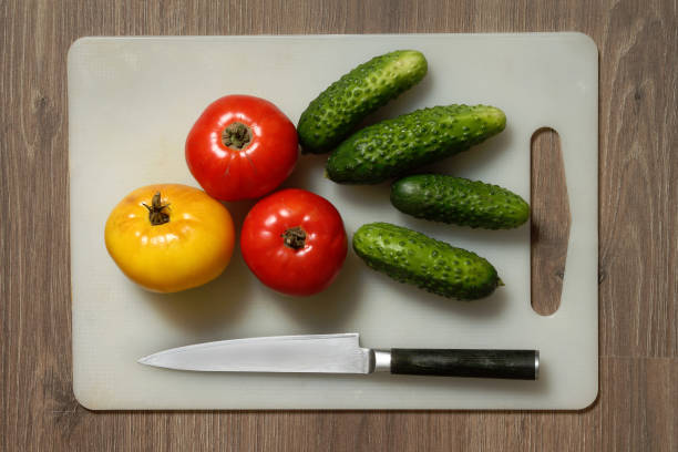 Tomato, cucumber and knife on cutting board. stock photo