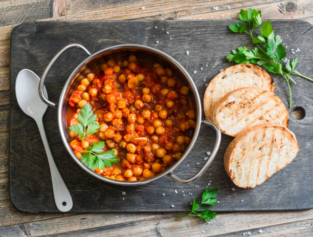Tomato sauce braised chickpeas in a pot, and grilled bread. Delicious vegetarian lunch on a rustic wooden background, top view stock photo