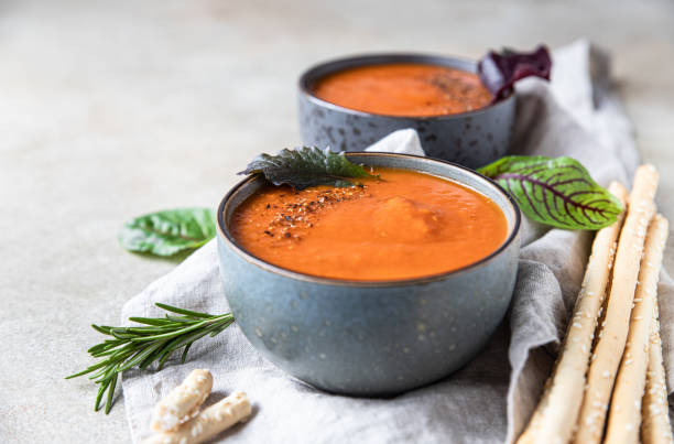 Tomato soup garnish with ground pepper, rosemary and bread sticks, light background. stock photo