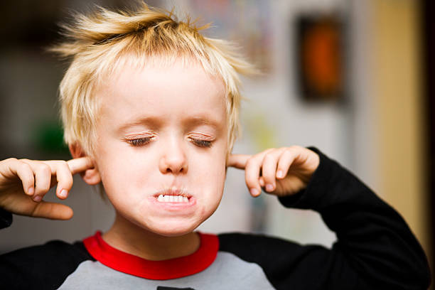 Too noisy! Small boy blocks his ears and screws up his face as he hears a loud sound. Fingers in Ears stock pictures, royalty-free photos & images
