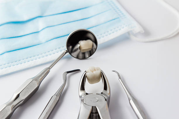 Tooth extraction concept Tooth extraction concept with an array of stainless steel dental tools and a mask with the extracted tooth clasped in the pincers and reflected in the mirror removing stock pictures, royalty-free photos & images