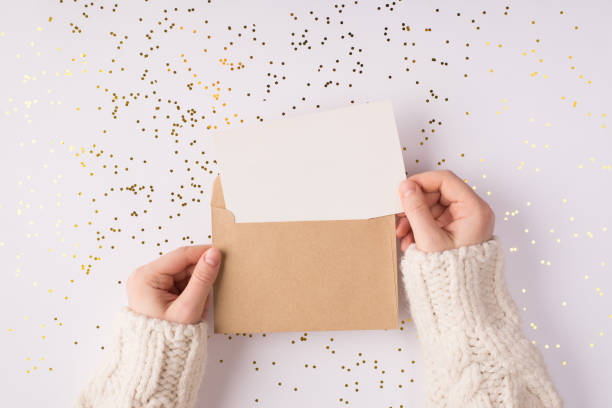 top above close up overhead view photo of female hands holding kraft paper envelope with mock up copy space card inside over shiny golden background table - woman holding a christmas gift imagens e fotografias de stock