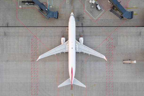 top down view on comercial airplane docking in terminal in the parking lot of the airport apron, waiting for services maintenance, refilling fuel services after airspace lock down. modern airliner - plane imagens e fotografias de stock