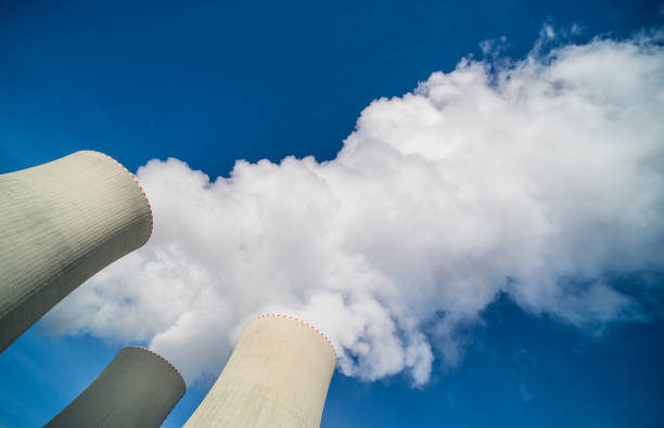 Top of nuclear power plant water cooling towers with white steam plume on a blue sky stock photo