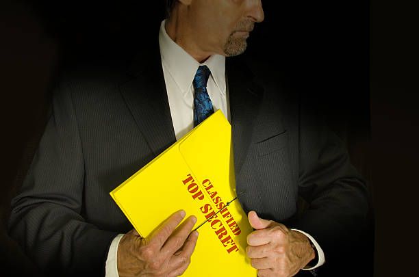 Top Secret Classified business and government concept Top Secret Classified business, legal and government concept showing a man in a black suit pulling a Top Secret folder dossier out of his jacket. Dramatic lighting highlights the Top Secret folder. top secret stock pictures, royalty-free photos & images