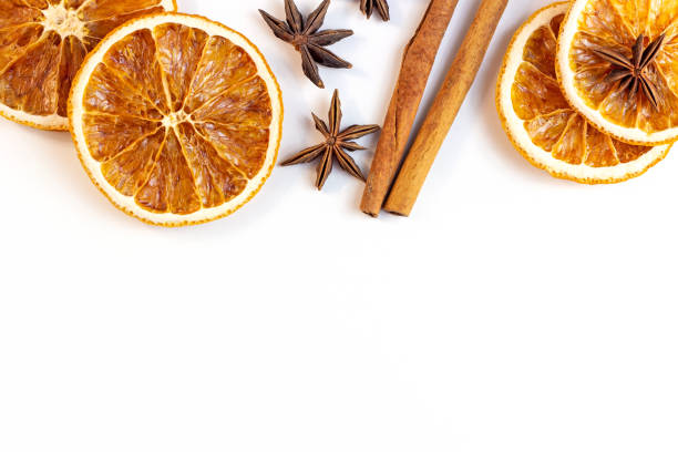 Top view flat lay of Christmas spices for traditional beverages: cinnamon sticks, anise stars, dry orange slices as a frame for Xmas seasonal decorations on white background with copy space stock photo