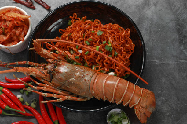 Top view Korean spicy dried instant noodle with painted spiny lobster and kimchi on black table background. Asian foods concept. stock photo