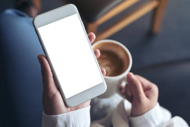 Top view mockup image of woman's hands holding white mobile phone with blank screen while drinking coffee in cafe Top view mockup image of woman's hands holding white mobile phone with blank screen while drinking coffee in cafe blank screen stock pictures, royalty-free photos & images