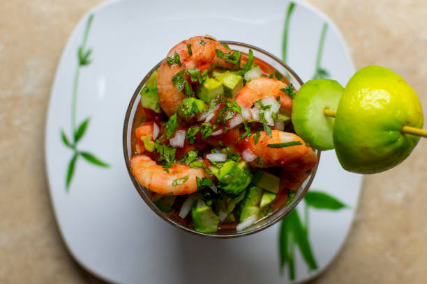 top view of a delicious shrimp cocktail with chopped onion, cilantro, avocado and lime, on a white plate with green. Fresh Mexican food top view of a delicious shrimp cocktail with chopped onion, cilantro, avocado and lime, on a white plate with green. Fresh Mexican food shrimp cocktail stock pictures, royalty-free photos & images