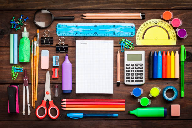 Top view of a large group of school or office supplies on wooden table Top view of a large group of multi colored school or office supplies shot on rustic dark wooden table. A blank note pad is at the center of the composition with useful copy space ready for text and/or logo. DSRL studio photo taken with Canon EOS 5D Mk II and Canon EF 100mm f/2.8L Macro IS USM stationary stock pictures, royalty-free photos & images