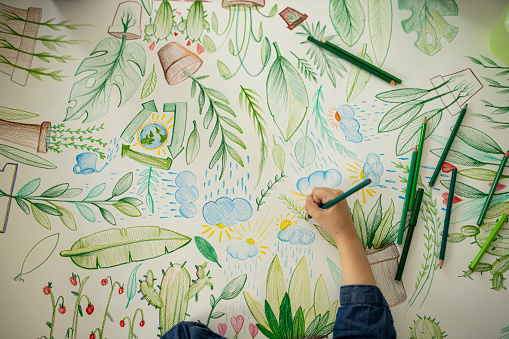 Photo of little girl, focus on hands, drawing plants and coloring on paper