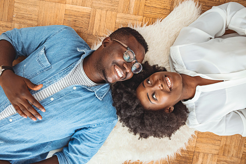 Top view of attractive African American couple lying on the floor. Young couple relaxing on the carpet, They are Happy, Smile and Laugh. Cozy Living Room with Modern Interior