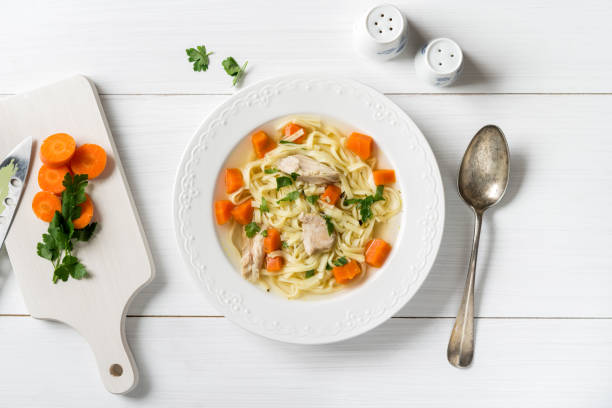 Top view of chicken soup with pasta, carrot and parsley on white table stock photo