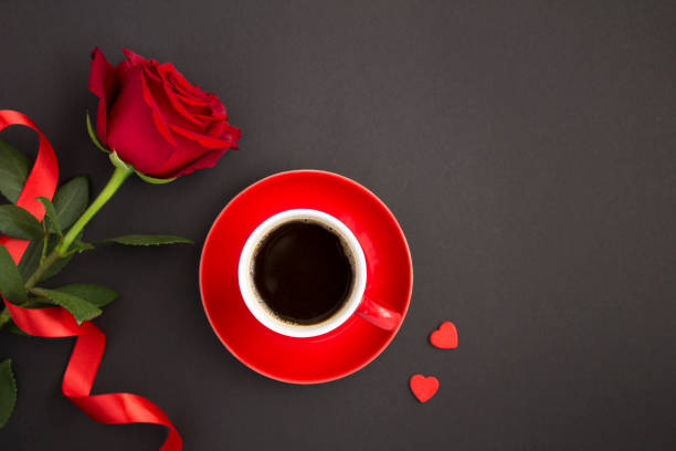 Top view of coffee in the red cup, rose and hearts on the black  background. Copy space. stock photo