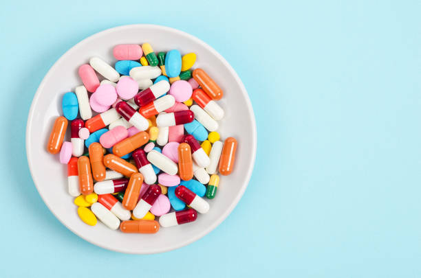 A top view of colourful medicine pills and capsules A top view of colourful medicine pills and capsules in white plate on blue background. Copy space for the ads. antihistamine stock pictures, royalty-free photos & images