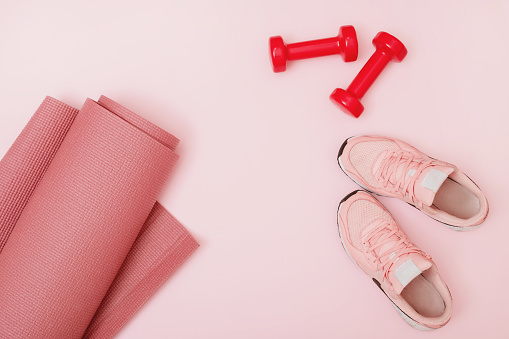 Top view of dumbbells, mat, and sneakers on pink background. Flat lay.