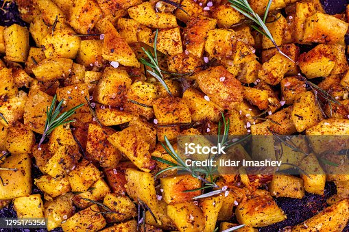 istock Top view of fresh baked pumpkin pieces with rosemary and spices on black metal pan background 1295175356