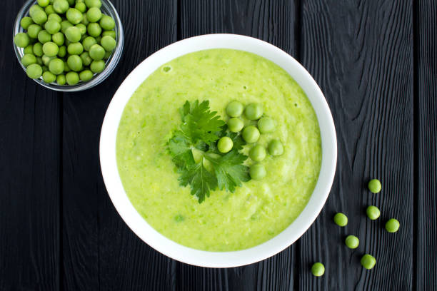 Top view of green pea soup  in the white bowl on the black wooden table stock photo