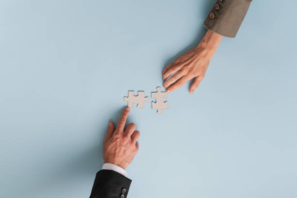 Top view of hands of businesswoman and businessman joining two  matching puzzle pieces Top view of hands of businesswoman and businessman joining two blank matching puzzle pieces. Over blue background with copy space. coalition stock pictures, royalty-free photos & images