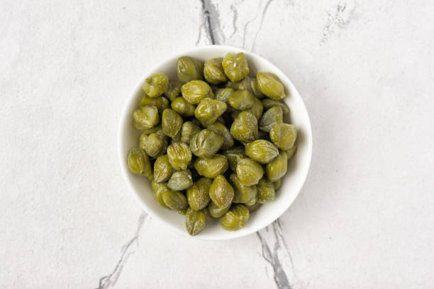 Top view of marinated caper flower buds in bowl Top view of marinated caper flower buds in bowl on white marble background caper stock pictures, royalty-free photos & images