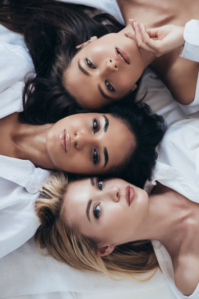 vista superior de tres atractivas mujeres multiétnicas mirando la cámara - belleza fotografías e imágenes de stock