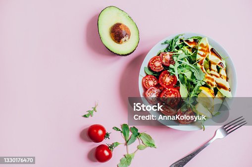 istock top view of tomato salad arugula avocado lemon in white plate on pink background 1330176470