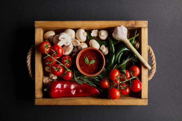 vue supérieure de la sauce tomate avec des feuilles de basilic près des tomates cerises, piments verts, champignons et romarin dans la boîte en bois sur le noir - champignon et en studio et fond noir photos et images de collection