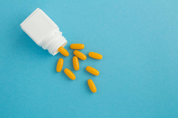 Top view of white bottle with the yellow pills on the blue  background. Copy space. stock photo