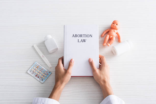 top view of woman holding book with abortion lettering near baby doll and abortion pills top view of woman holding book with abortion lettering near baby doll and abortion pills abortion pill stock pictures, royalty-free photos & images