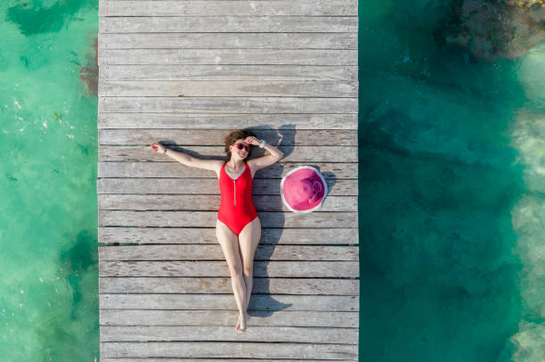 Top view of woman lying down on wooden pier at sunny summer day in Cancun, Mexico. Young woman in the red swimwear on Caribbean. Summer beach vacation concept stock photo
