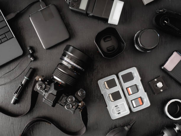 top view of work space photographer with digital camera, flash, cleaning kit, memory card, external harddisk, USB card reader, laptop and camera accessory on black table background stock photo