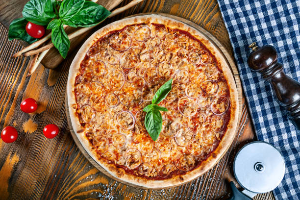 Top view on homemade fresh italian tuna pizza. Pizza on rustic background with tomato, basilic. Copy space. Traditional italian cuisine. stock photo