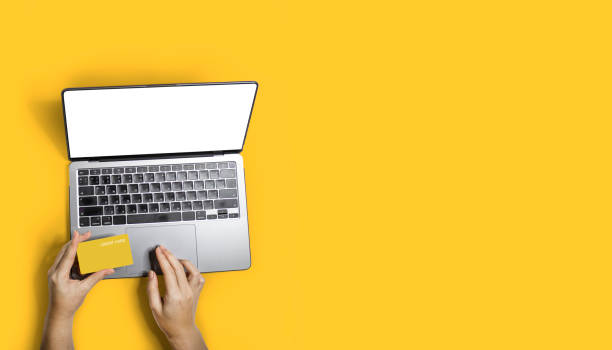 Top view person shopping online with their laptop and using a yellow credit card to pay for products. stock photo