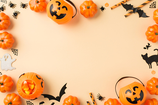 Top view photo of halloween decorations pumpkin baskets candy corn straws spiders web bats ghost and black cat silhouettes on isolated beige background with copyspace in the middle