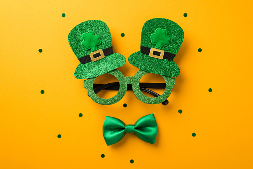 Top view photo of st patrick's day decorations funny outfit hat shaped party glasses and green bow-tie on isolated yellow background