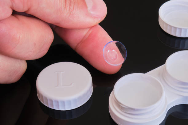Toric contact lens on fingertip with white contact lens case and cap - composition on black reflective background. stock photo