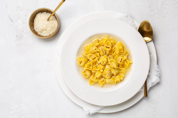 Tortellini. Pasta stuffed with a mix of meat, and parmigiano cheese and served in capon broth. Top view, white background. stock photo