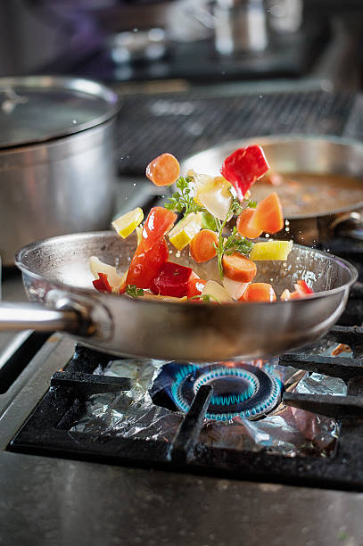 Tossing fresh vegetables in saucepan at kitchen Restaurant. Shallow DOF. Developed from RAW; retouched with special care and attention; Small amount of grain added for best final impression. 16 bit Adobe RGB color profile. camping stove stock pictures, royalty-free photos & images