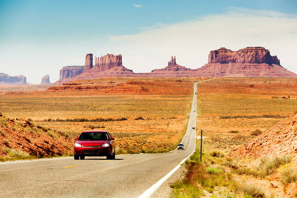 Touring the American Southwest, Monument Valley Highway with Cars Subject: Tourists in a red car traveling in the American Southwest, driving downhill on a straight length of highway stretching from southern Utah toward Monument Valley, Arizona colorado plateau stock pictures, royalty-free photos & images