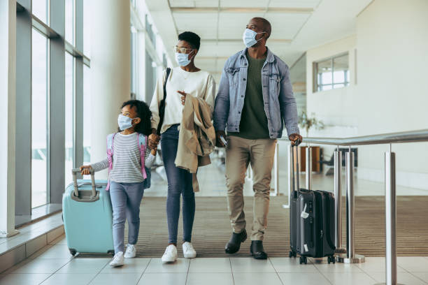 Tourist family walking through passageway in airport Tourist family walking through passageway in airport. Young girl with family in face masks walking with luggage in airport corridor. south africa covid stock pictures, royalty-free photos & images