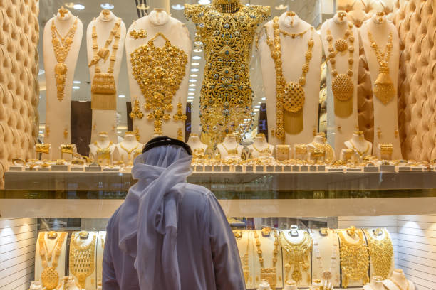 A tourist is busy for exploring heavyweight expensive gold jewellery at Dubai Gold Souk in Dubai, UAE. The Gold Souk stores also offer platinum, diamonds and occasionally silver, and the government keeps tight control over the quality. A man with traditional was exploring traditional gold ornament at the Dubai Gold Souk in Dubai. Dubai Gold Souk situated at the commercial business district in Deira, in the locality of Al Dhagaya. The souk consists of over 380 retailers, most of whom are jewelry traders. The Gold Souk stores also offer platinum, diamonds and occasionally silver, and the government keeps tight control over the quality of all the merchandise, so rest assured that your purchases will be genuine. souk stock pictures, royalty-free photos & images