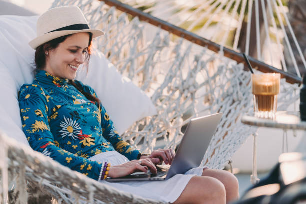 Tourist on summer vacation combining work and leisure Woman on beach holiday resting in hammock and working on laptop nomadic people stock pictures, royalty-free photos & images