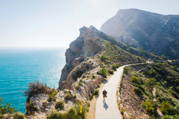 Tourist walking on scenic walking path along steep cliffs along the ocean in the natural park 'Serra Gelada' in Albir, Spain stock photo