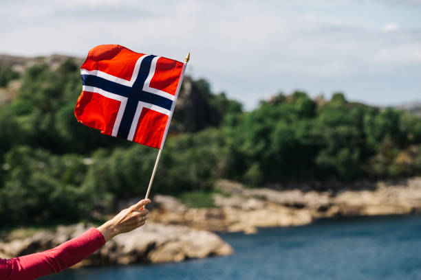 Tourist with norwegian flag on sea coast Tourist hand holding norwegian flag on rocky stone sea coast background. norway stock pictures, royalty-free photos & images