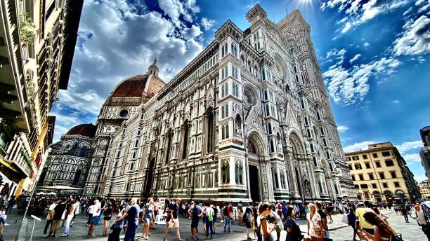tourists flood the streets of florence as the line for the florence cathedral tour wraps around and encompasses the building. (wide angle view) stock photo